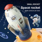 White plastic rocket water sprinkler toy with red top and astronaut decal, launching from a yellow planet-like base.