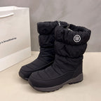 Black mid-calf snow boots with quilted fabric, a fuzzy lining, side zipper, and a circular snowflake emblem patch.