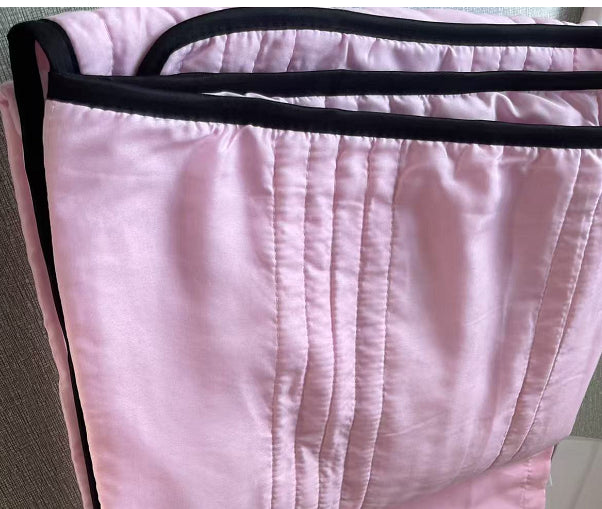 Soft pink cooling summer quilt with vertical stitching and contrasting black trim edges.