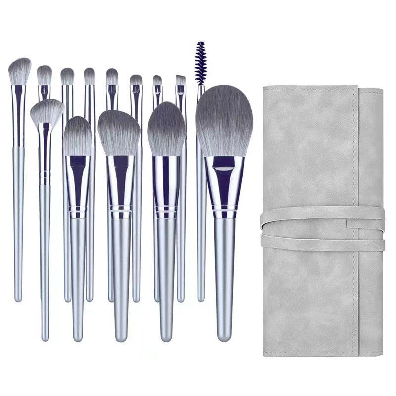 A set of 11 silver-handled makeup brushes with soft grey bristles and a matching grey roll-up storage case.