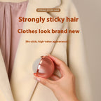 Hand holding a rose-gold, spherical, reusable gel lint remover ball against a cream-colored coat.