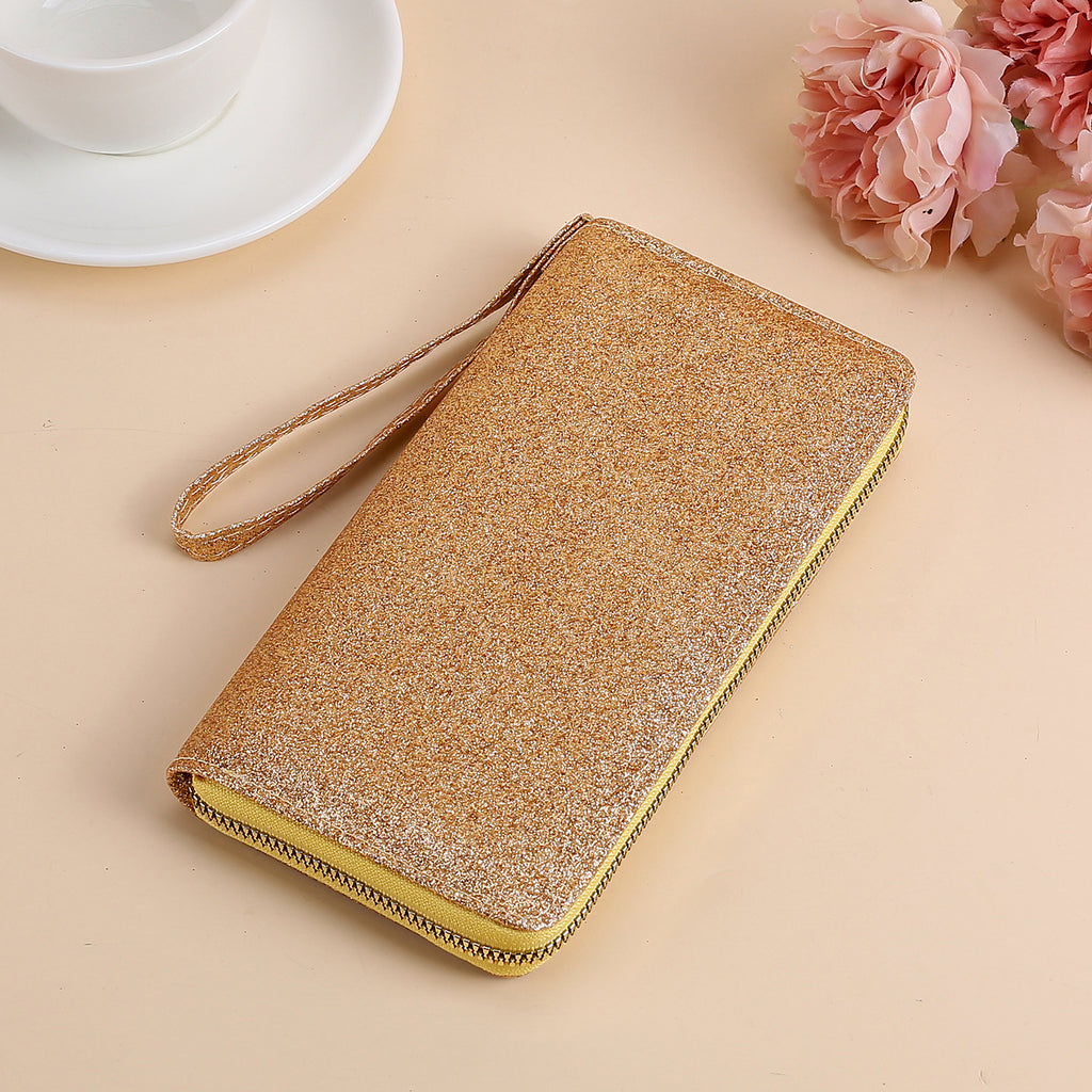 Gold glittery zip-around women's clutch with a matching wrist strap, set on a beige surface with floral accents.