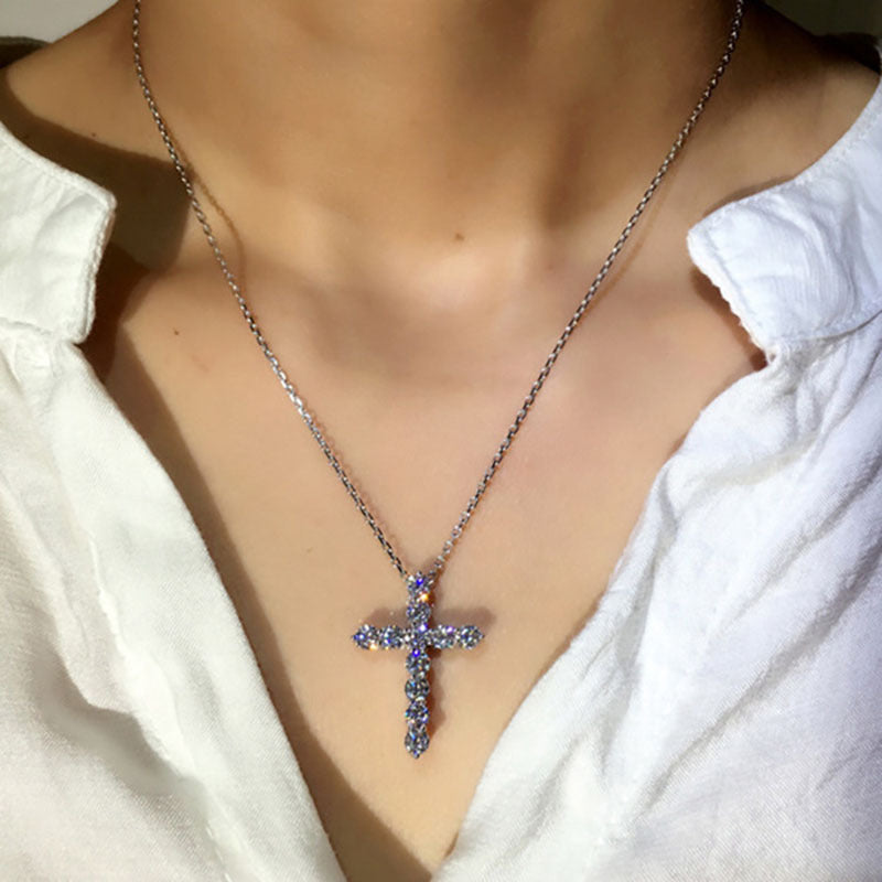 Silver necklace featuring a sparkling diamond-encrusted cross pendant, worn on a person in a white collared shirt.