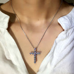 Silver necklace featuring a sparkling diamond-encrusted cross pendant, worn on a person in a white collared shirt.