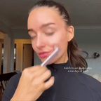 A person uses a sleek, portable pink facial rejuvenation wand with LED light therapy on their cheek.