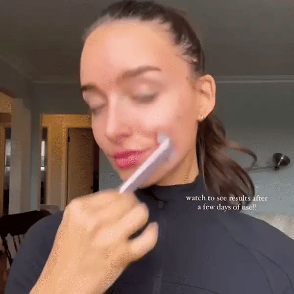A person uses a sleek, portable pink facial rejuvenation wand with LED light therapy on their cheek.