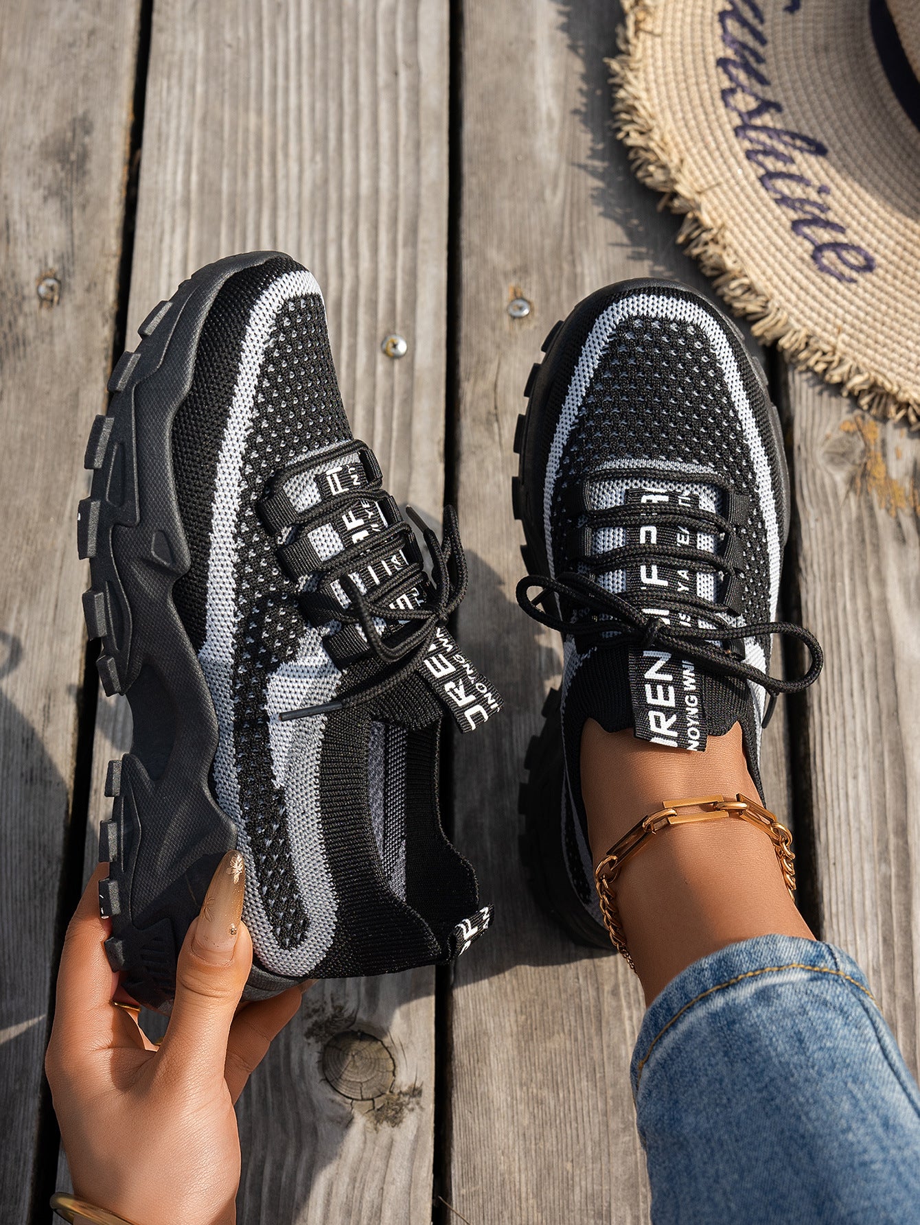 Black and white flyknit mesh sneakers with chunky soles, lace-up fronts, and branded tongues on a wooden deck.