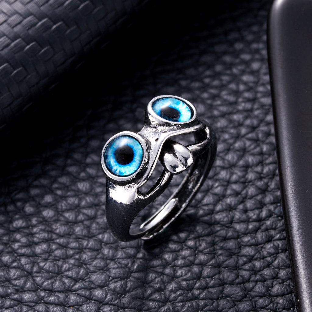 Silver frog-style hip hop ring featuring two prominent, vibrant blue glass cat-eye cabochons on a black leather surface.