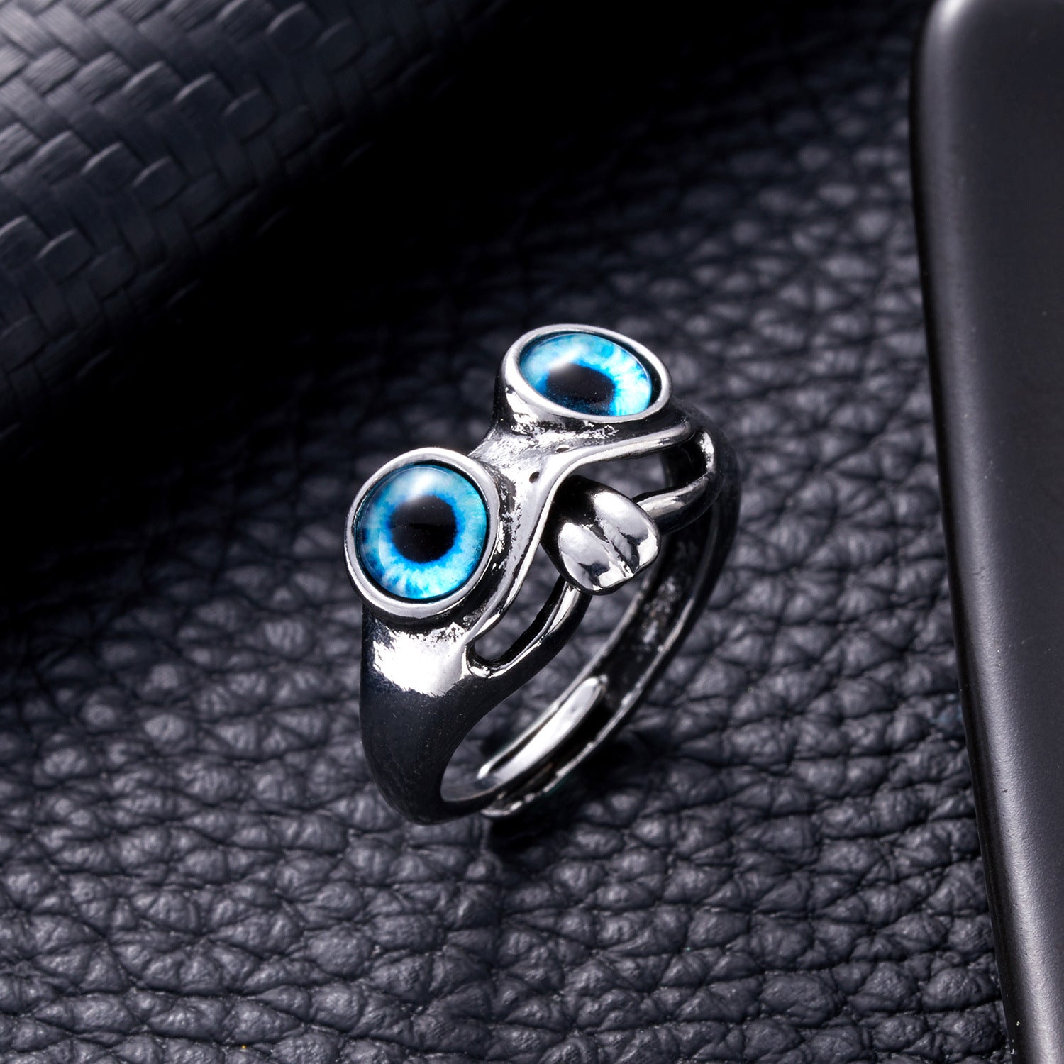 Silver frog-style hip hop ring featuring two prominent, vibrant blue glass cat-eye cabochons on a black leather surface.