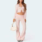 A model wearing a light pink slim-fit hooded cropped zip-up jacket with ribbon ties and matching flared ribbed pants.