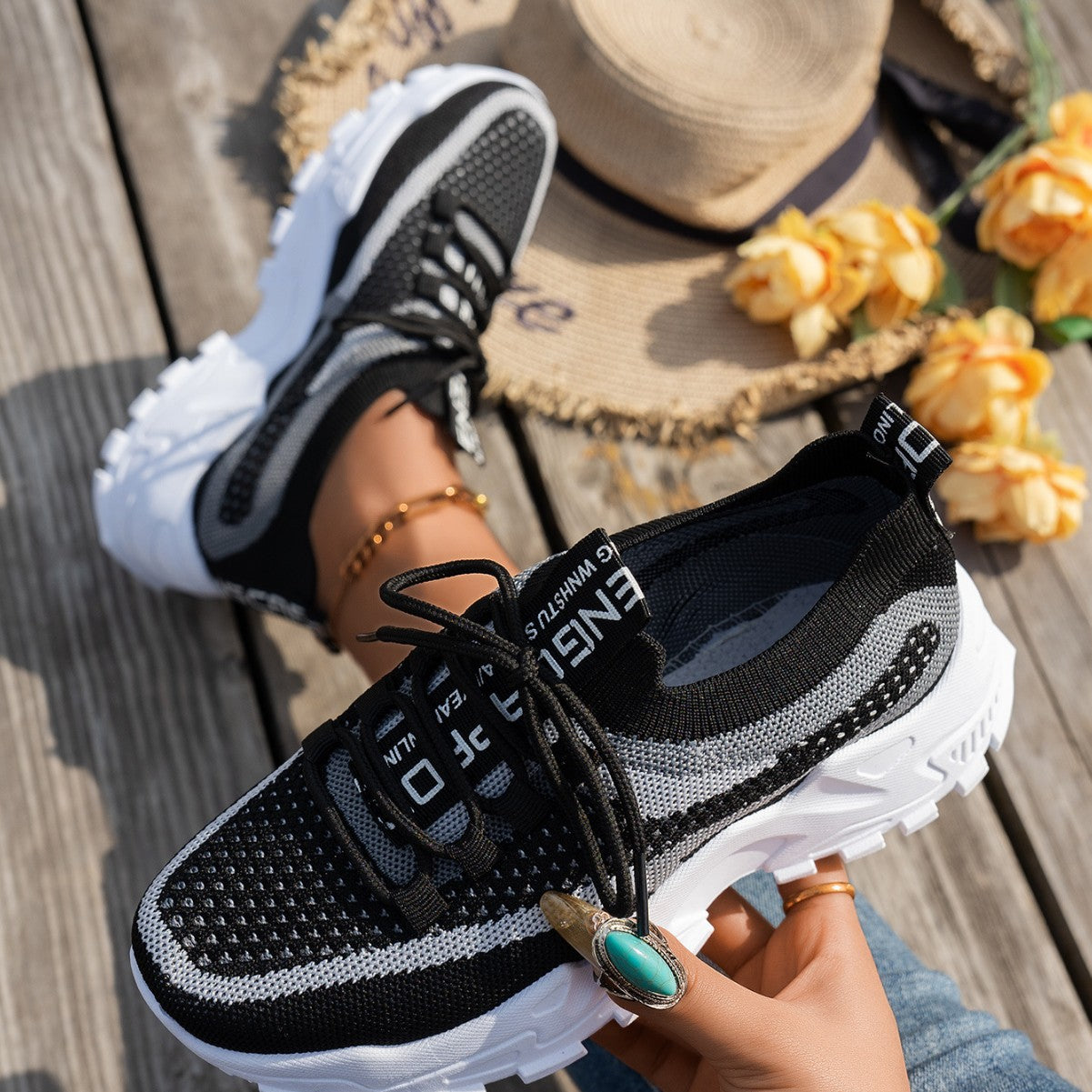 Black and grey women’s flyknit mesh sneakers with lace-up fronts and thick white chunky soles on a wooden background.