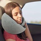 A woman sleeping in a car wearing a soft, grey fabric cervical neck pillow for support.