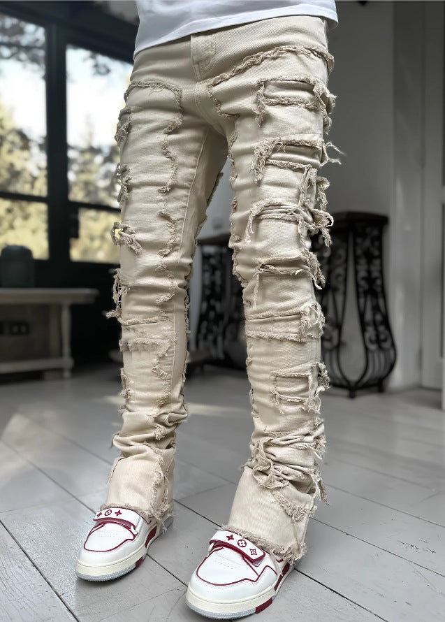 Beige stacked denim jeans featuring distressed horizontal rips with frayed edges, worn with white and red sneakers.