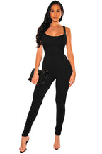 Woman wearing a black, form-fitting sleeveless exercise jumpsuit, holding a matching black clutch bag.