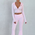 A woman wears a light pink, slim-fit knit zip-up hoodie and matching high-waisted flared pants.