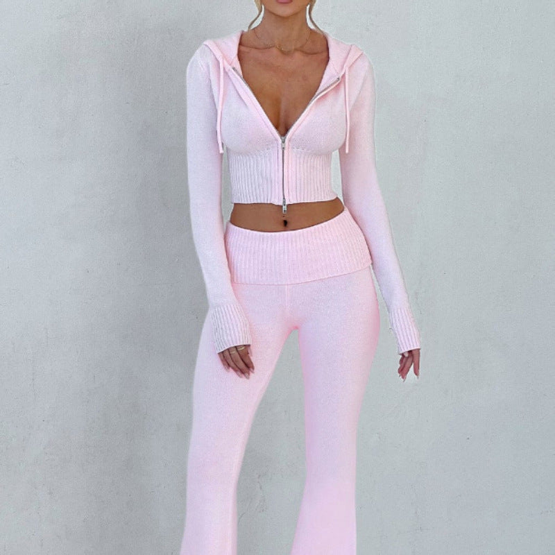 A model wearing a light pink, slim-fit, ribbed knit set: a hooded zip-up crop top and matching flared trousers.