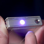 Silver metallic playing-card style lighter with a bright blue LED light feature, held between fingers.