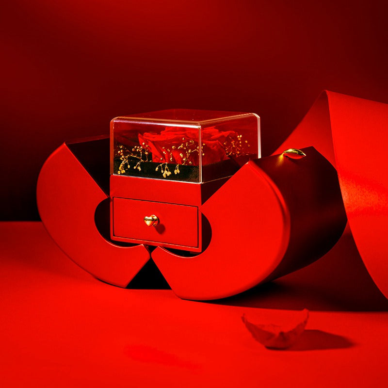 Red apple-shaped gift box with a drawer and clear case containing an eternal rose on a red background.