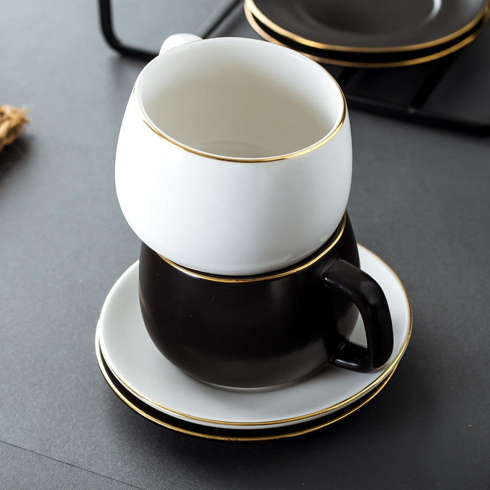 Stacked white and black matte ceramic coffee cups with gold rims, resting on matching saucers on a dark surface.