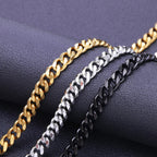 Gold, silver, and black metal Cuban link chains displayed diagonally on a dark textured surface.