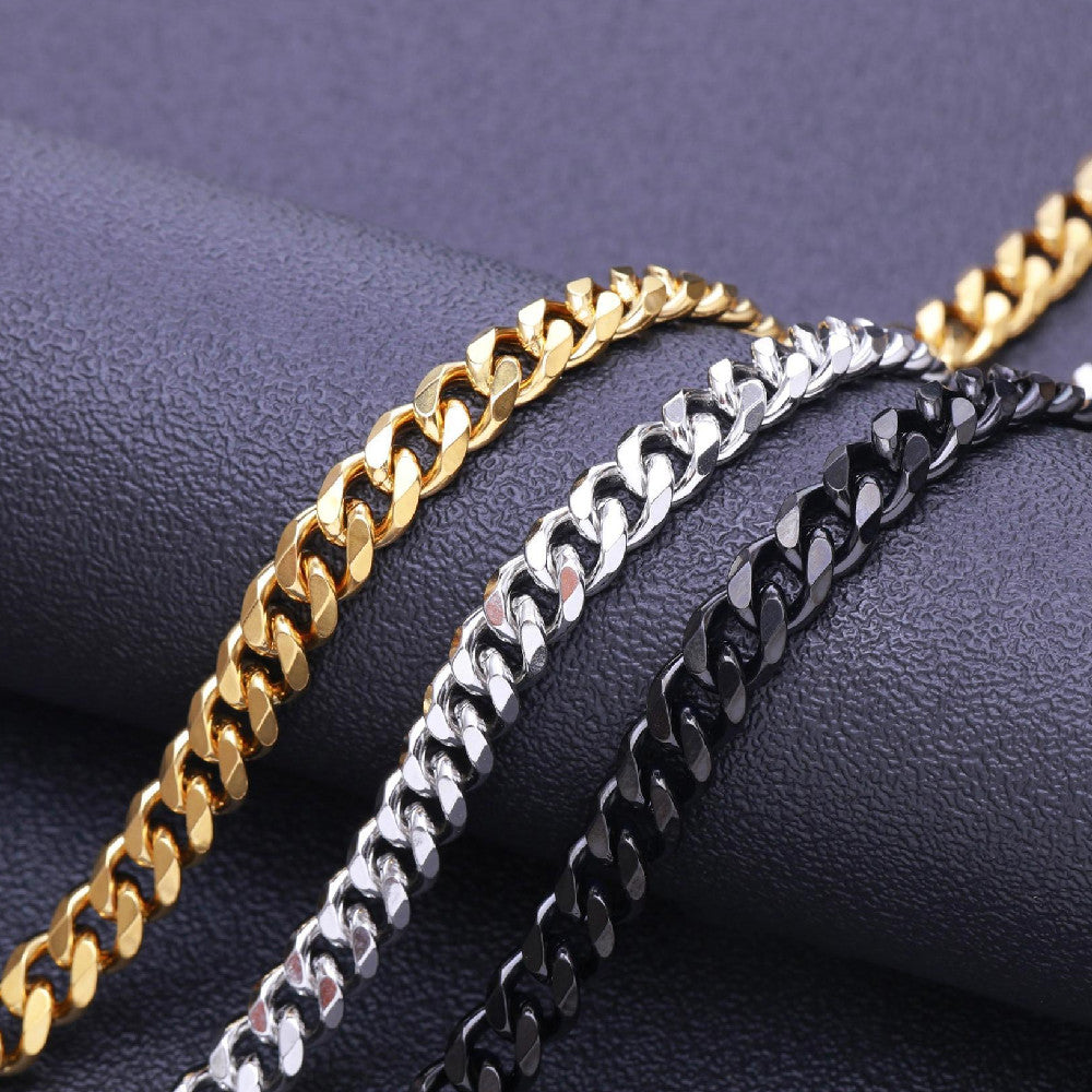 Gold, silver, and black metal Cuban link chains displayed diagonally on a dark textured surface.
