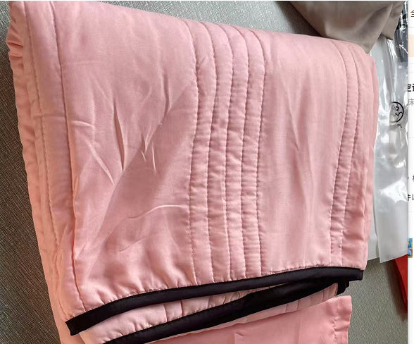 Folded light pink summer cooling quilt with vertical stitching and dark brown trim.