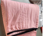Folded light pink summer cooling quilt with vertical stitching and dark brown trim.