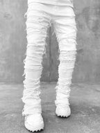 White stacked denim jeans with heavy distressing, frayed ripped details, and a slim, long-fit silhouette for men.