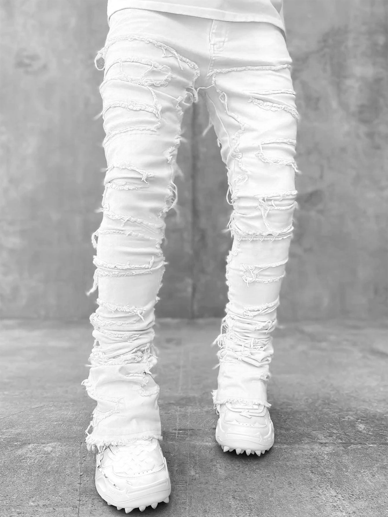 White stacked denim jeans with heavy distressing, frayed ripped details, and a slim, long-fit silhouette for men.