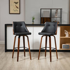 Two modern swivel bar stools with black faux leather seats, tufted backs, and walnut wood legs with black metal supports.