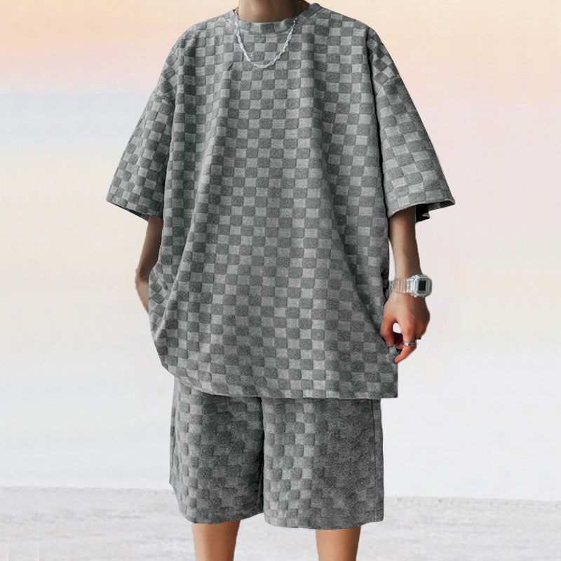 A person wears a grey, loose-fit jacquard plaid short-sleeve shirt and matching casual straight shorts.