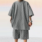 A person wears a grey, loose-fit jacquard plaid short-sleeve shirt and matching casual straight shorts.