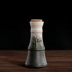 A tapered, ceramic sake pot fades from dark green to cream, featuring a leaf design and a small cork stopper.