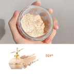 Hand holding Maco Andy finishing powder jar with pale peach powder and a gold ballerina-themed cosmetic container.