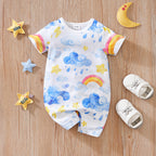 White short-sleeve baby romper with watercolor blue clouds, rainbows, yellow stars, and snaps on a wooden background.