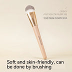 Uodo foundation brush with a flat, soft grey-white head, gold ferrule, and a beige handle on a neutral background.