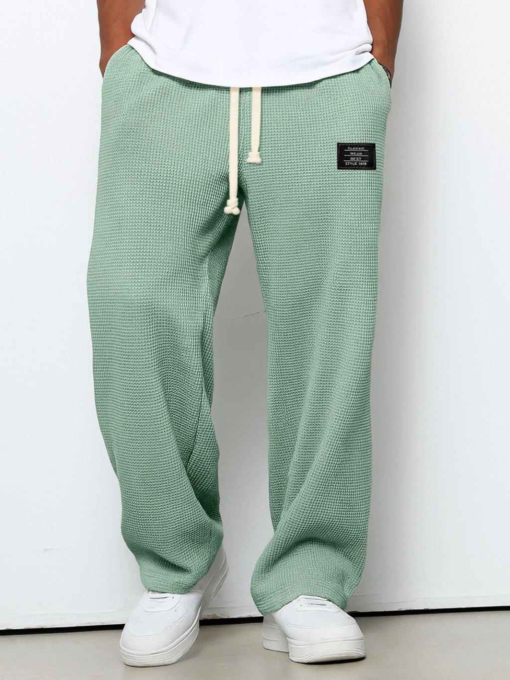Men wearing loose, sage green waffle-knit straight pants with a drawstring waist and a small black brand patch.