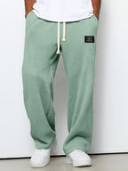 Men wearing loose, sage green waffle-knit straight pants with a drawstring waist and a small black brand patch.