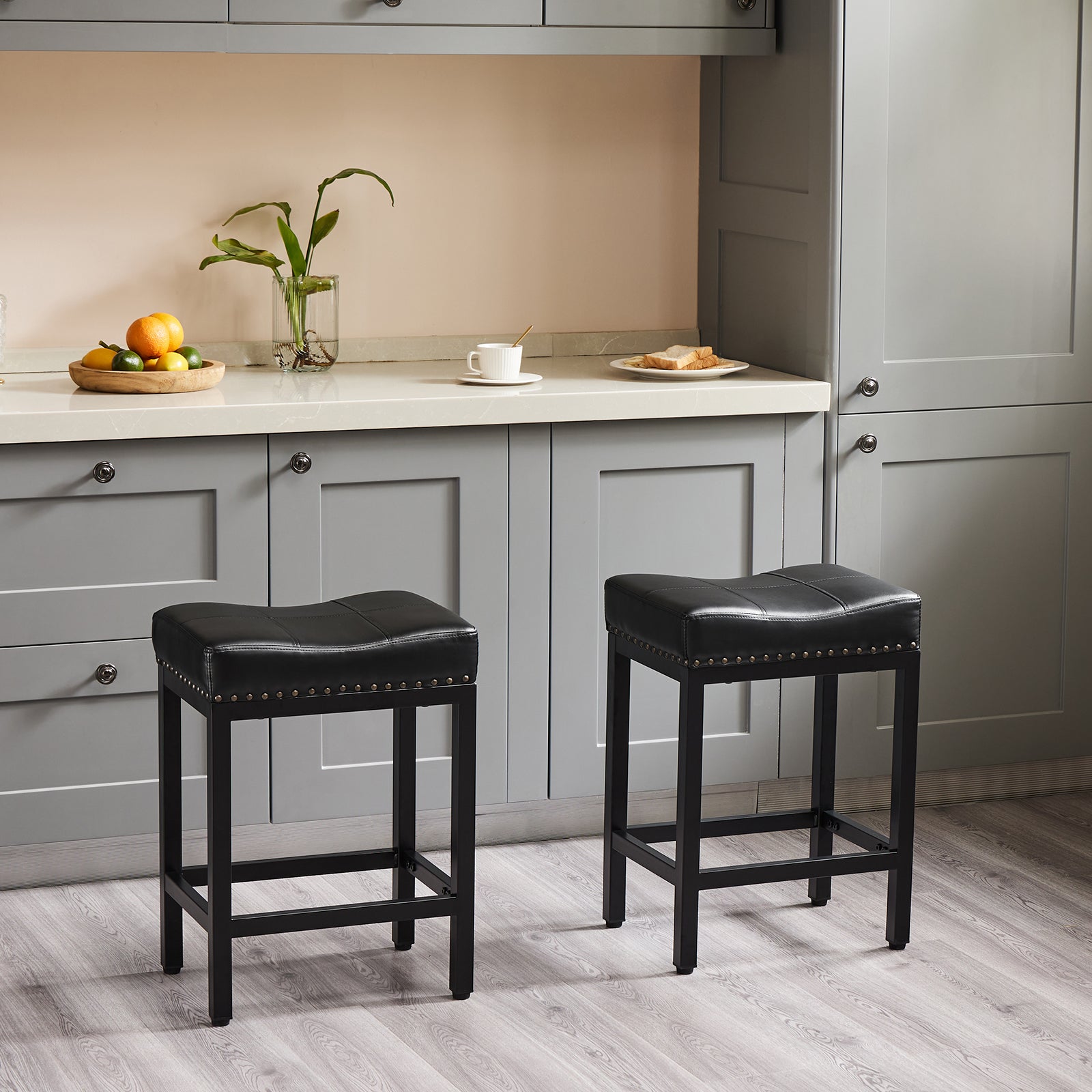 Two black saddle-seat stools with sturdy steel frames and nailhead trim in a modern kitchen.