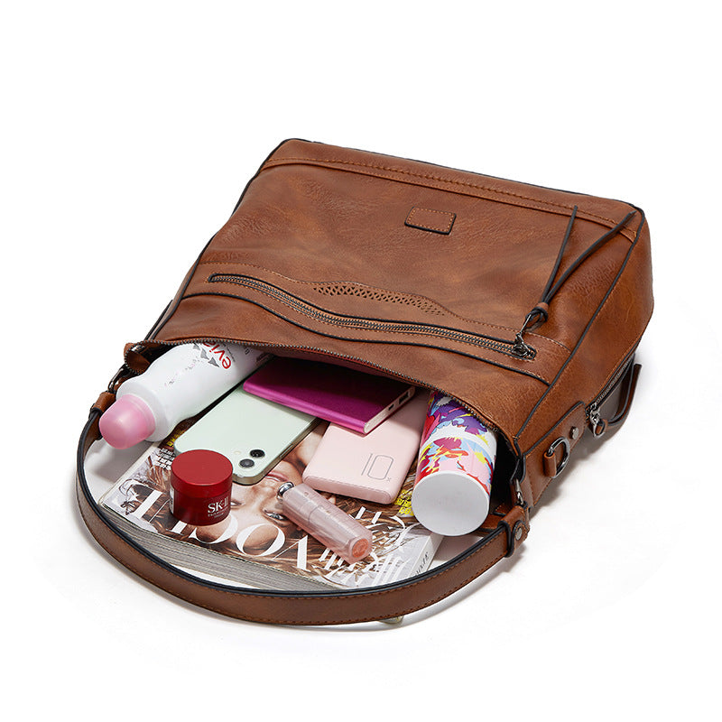A vintage-style brown leather one-shoulder tote bag, shown open and filled with personal items on a white background.