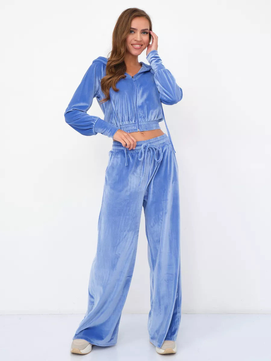 A woman wears a blue velour two-piece set: a cropped zip-up hoodie and matching wide-leg trousers with a drawstring.