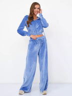 A woman wears a blue velour two-piece set: a cropped zip-up hoodie and matching wide-leg trousers with a drawstring.