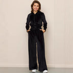 Woman wearing a black velour hooded zip-up jacket and matching wide-leg trousers with a drawstring waist.