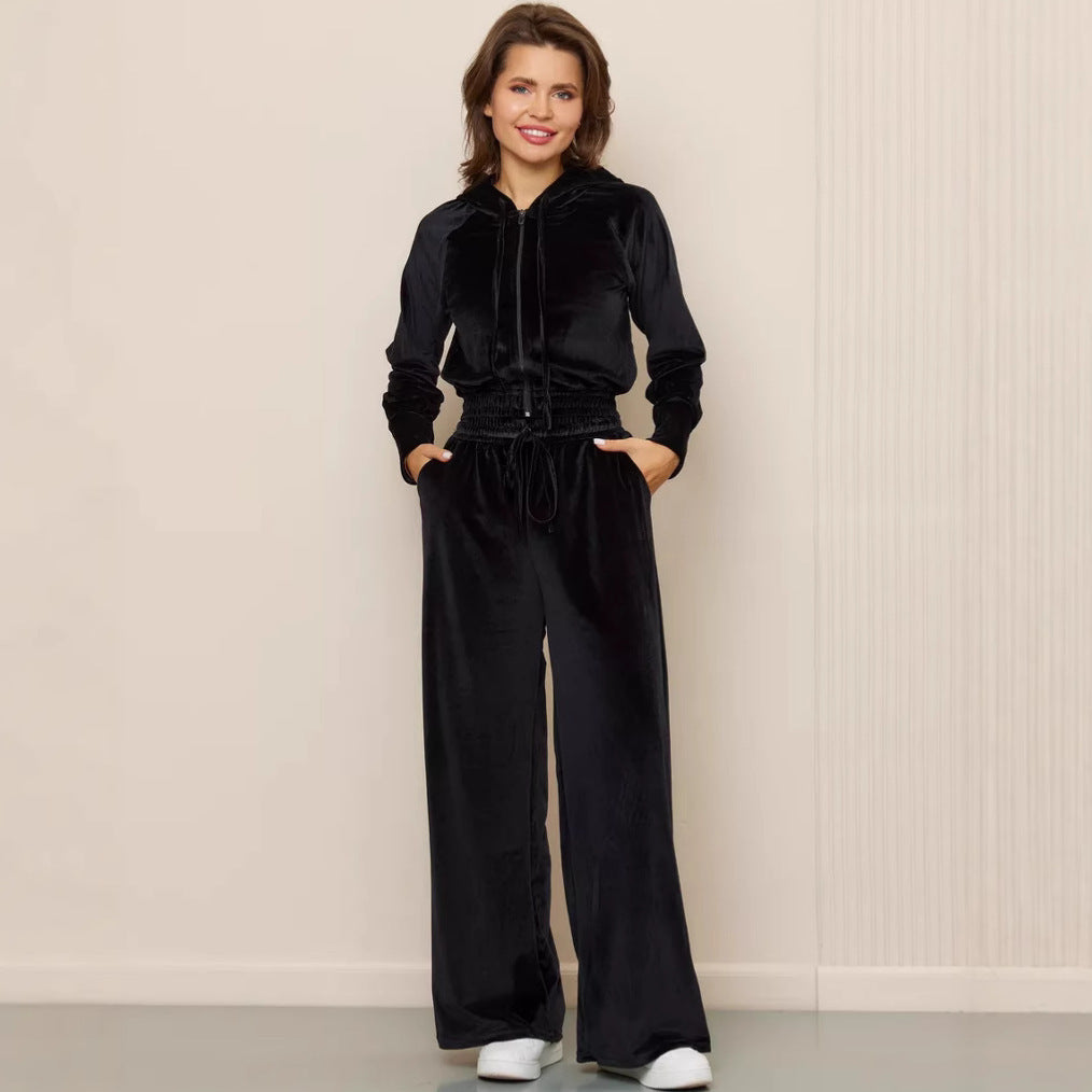 Woman wearing a black velour hooded zip-up jacket and matching wide-leg trousers with a drawstring waist.