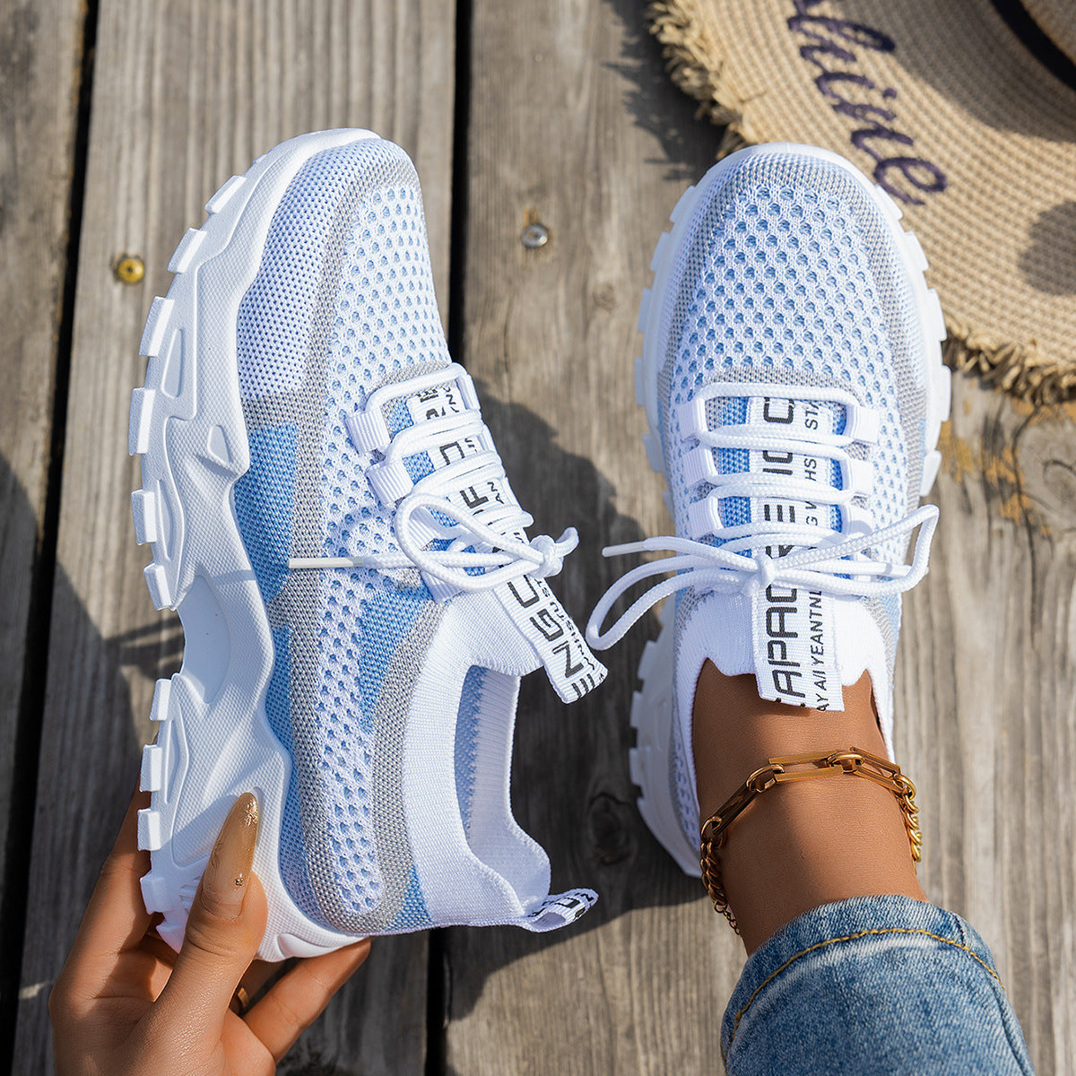 White and blue breathable mesh sneakers with chunky white soles, lace-up fronts, and branded straps on wood background.