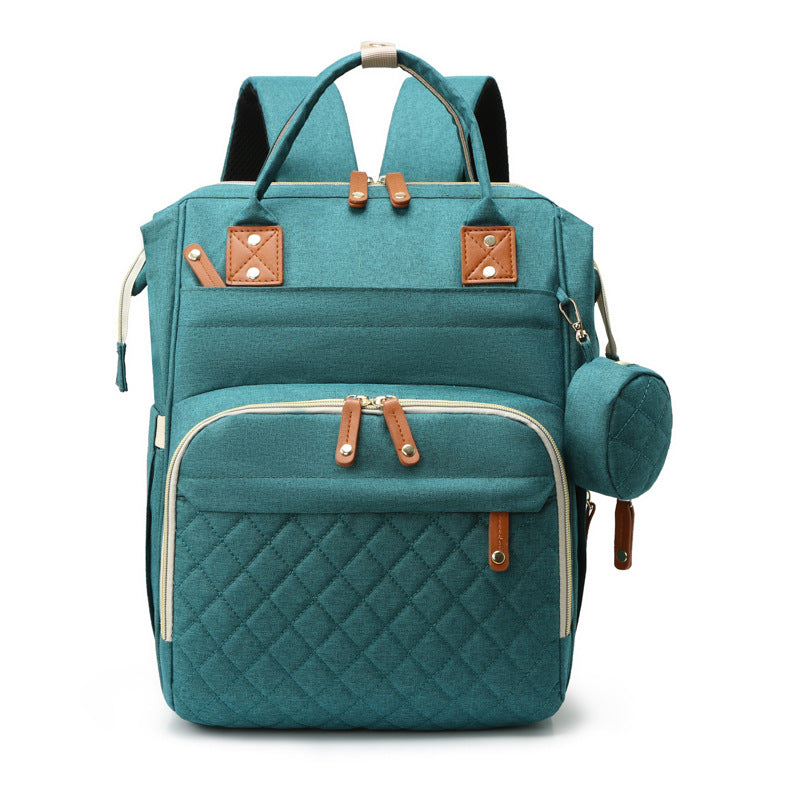 Teal fabric mummy backpack with quilted front pocket, brown leather-style accents, top handles, and small side pouch.