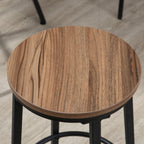 Close-up of a round bar stool with a brown wood-grain top and a sturdy black metal frame.