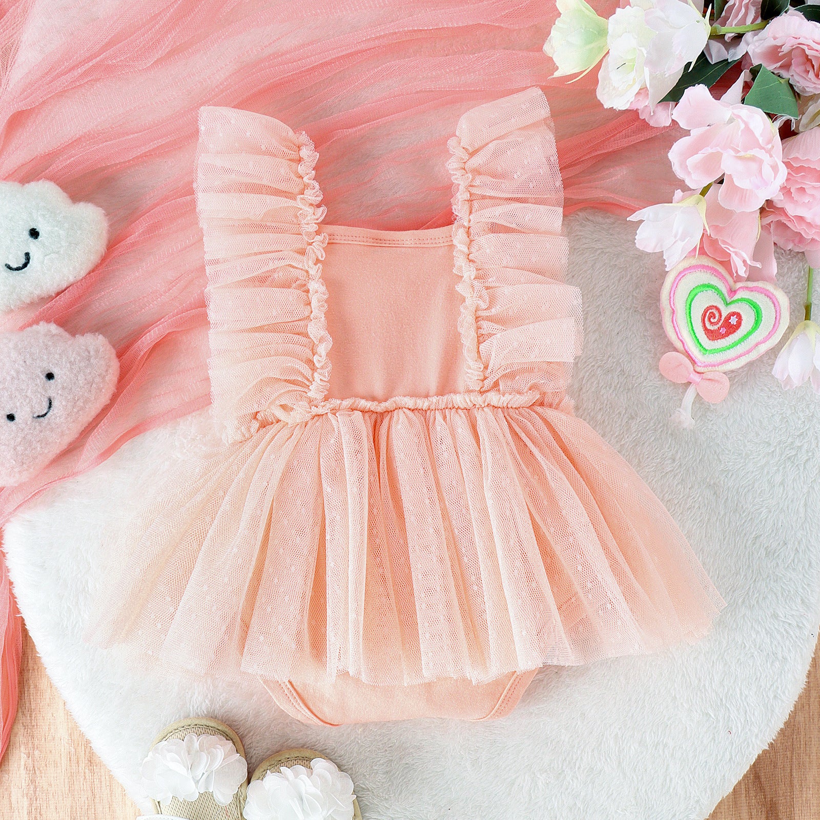 Peach baby jumpsuit with ruffle-trimmed straps and a sheer polka-dot tulle skirt overlay.