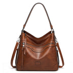Brown vintage-style soft leather tote with zipper pockets, top handle, and detachable shoulder strap on white background.