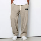 Loose beige waffle-knit trousers with a drawstring waist, side pockets, and a small black patch label.